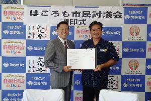 結城 和昭理事長と市長が市民討議会協定書をもって立っている写真