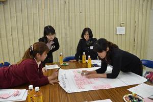 テーブルの上に広げた模造紙を見ながら発表に向けて意見をまとめる4人の参加者の写真