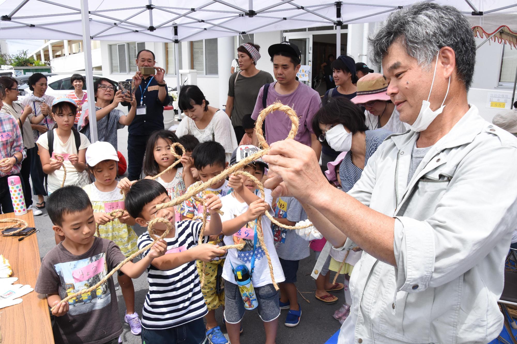 綱をもって子供たちに見本を見せている男性と綱をもって男性の真似をしている子供たちの写真