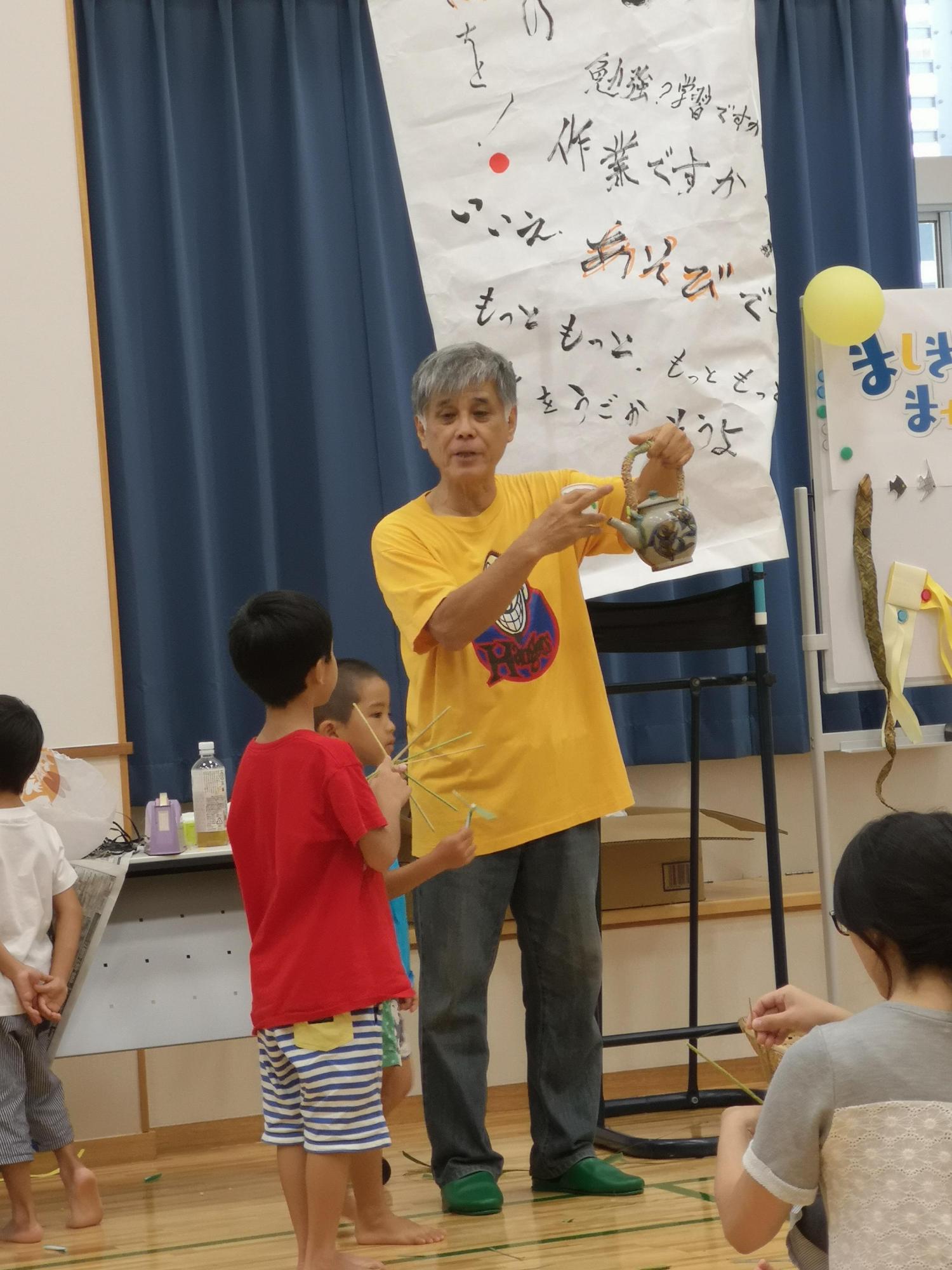 急須を手に持って立っている講師の男性と横に立っている2人の男の子の写真