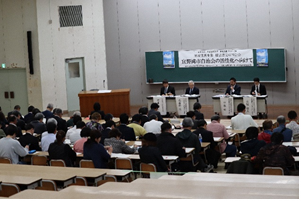 4名の報告者が前方に座り、報告会に参加した人々を後方から撮影した会場内の写真