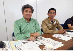 宅建業者会の2名の男性が机の上にたくさんの資料がおかれのている部屋での写真