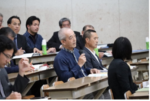 報告会に参加した男性が着席しながらマイクを右手で持ち意見を述べている写真