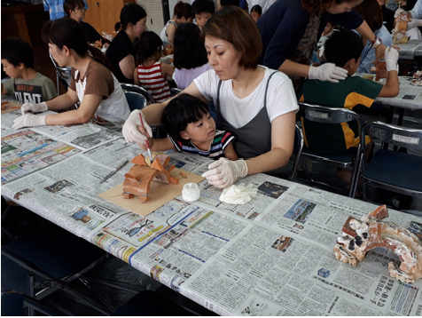 小さな子供を膝に抱えた母親が作品に絵を描いている写真