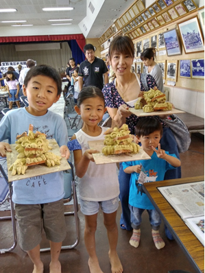 お母さんと男の子、女の子が出来上がった作品を持ち、お母さんの前で小さな男の子がピースサインをしている写真