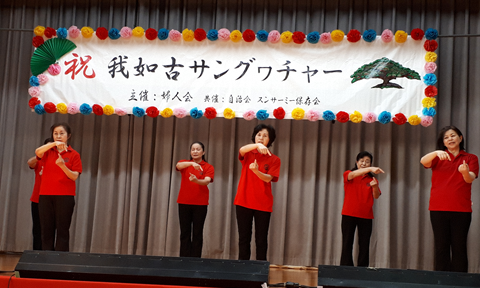 黒のズボンに赤のシャツをきた6人の女性が舞台上で手話をしている写真