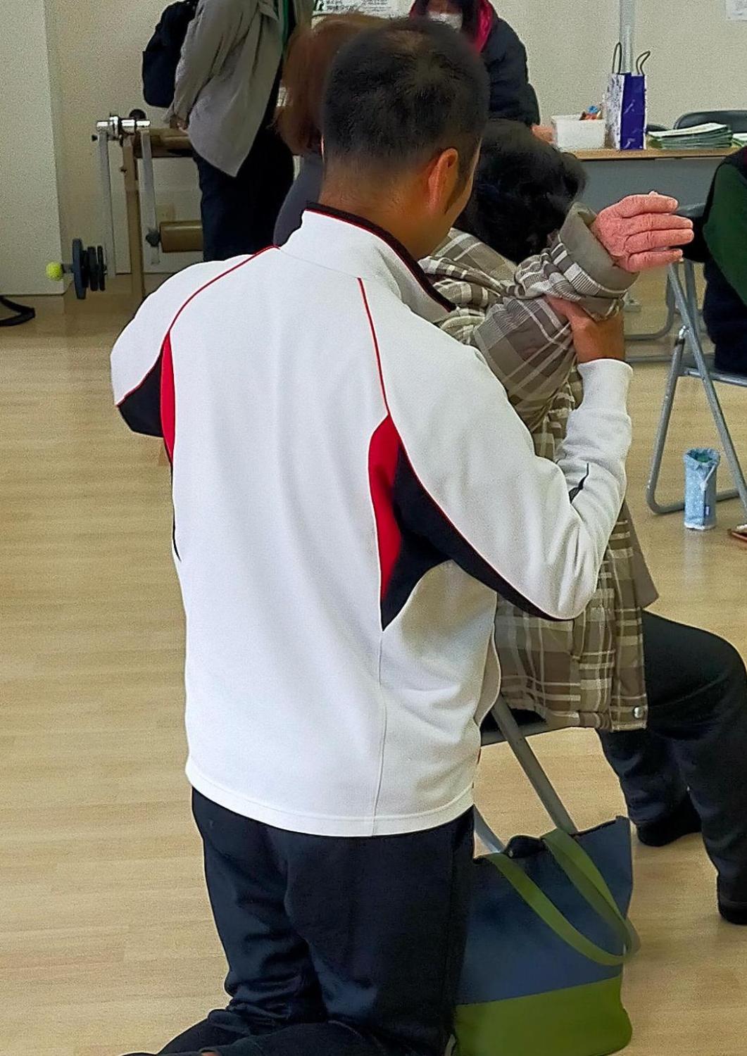 疼痛改善教室。個別指導中。指導者は参加者の背後に立ち、参加者の肩の動きを確認している。