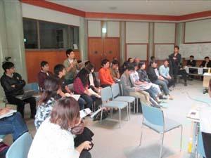 学生の皆さんが椅子に座り代表の方がマイクを持って意見を発表している写真