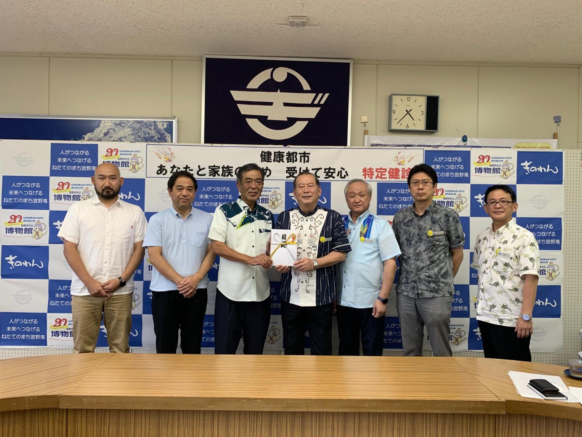 目録を持っている松川市長と宜野湾市建築設計事務所会関係者の方々の写真