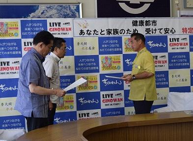 男性2名が並び1名の方に文書を手渡しそうしている写真