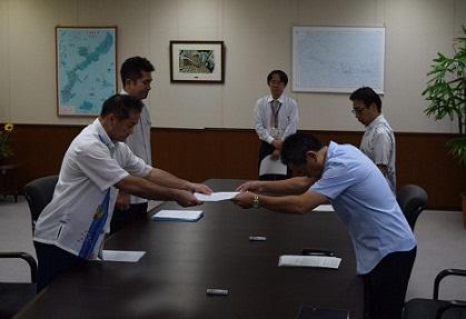 ブルーのシャツの男性が、市長へ書類を頭を深々と下げて両手で渡している写真