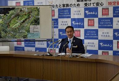 机に座り4台のマイクの前で記者会見を行っている市長の写真