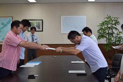 2名ずつの関係者が向かい合い市長から抗議・要望文書を手渡している写真