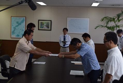 5名の関係者が向かい合って立ち市長が抗議・要請文書を手渡している写真