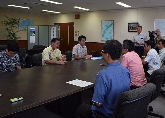 机を囲んで8名で会議をしている写真