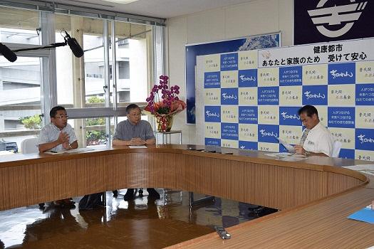 男性2名と市長が円状の机に座り、市長が資料に目を通している写真