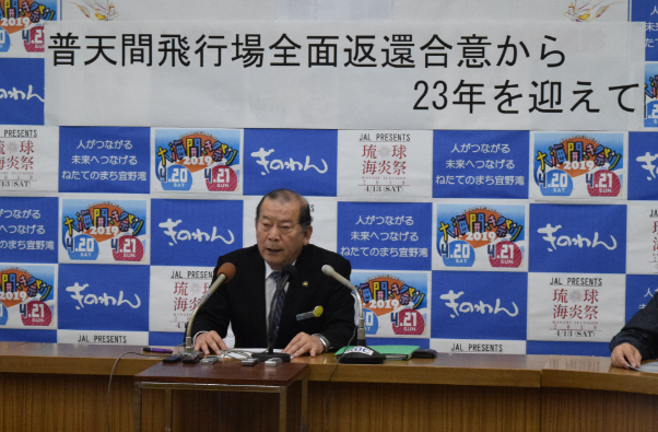 普天間飛行場全面返還合意から23年を迎えてと書かれた横断幕が張られたパネルの前に座り話しをしている市長の写真