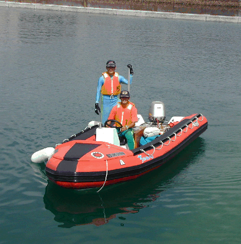 オレンジ色の救護ベストを着た男性2人が救助艇ゴムボートへ乗って記念写真