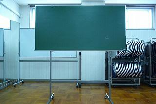 部屋に黒板が置いてあり、後方にはパイプ椅子が整頓されている写真