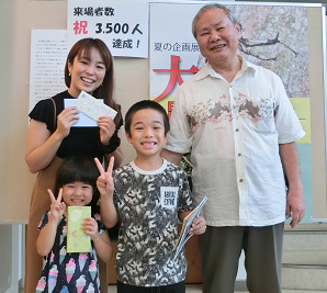 記念品を手に持った高江洲さんご一家と千木良館長の記念写真