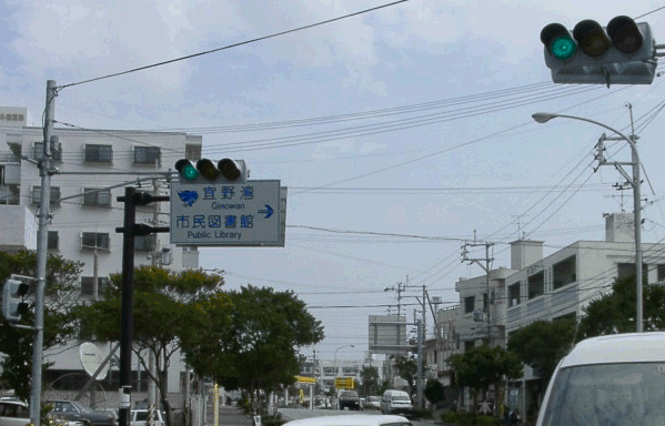信号機の下にある「宜野湾市立図書館」の案内版の写真