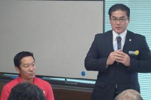 起立して挨拶をする市長と、その横に座っている宜野湾青年会議所結城理事長の写真