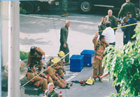 茶色の防火服を着た消防隊員の男性達がアスファルトの上に座っている写真