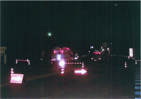 真っ暗な道路で赤と白のコーンや方向指示版などが光っている写真