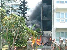 マンションの階段周辺が火事で焼けて黒い煙が上がっている様子を軍人の男性たちが見ている写真