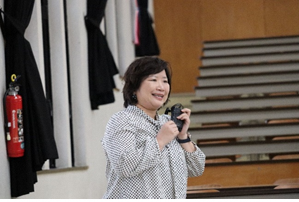 報告会に参加した女性が左手でマイクを持って話をしている写真