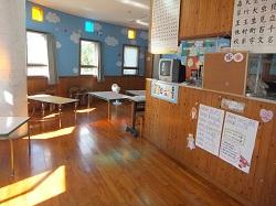 木製のフローリングと壁で机が並べられている学童室室内の写真
