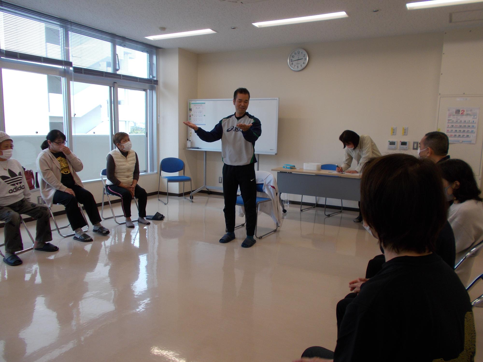 がんじゅう広場。指導者が動作法についてお話している。参加者は円になってお話を聞いている。