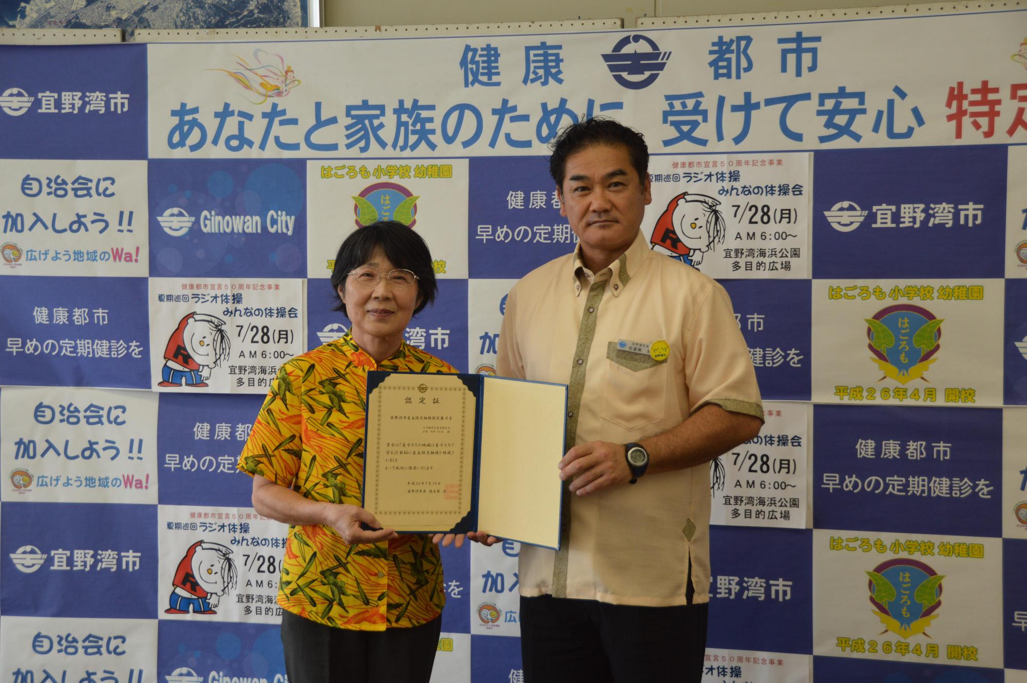 自主防災組織認定証授与式にて上大謝名自治会大城 ちえ子会長と市長が認定書を手に記念撮影している写真