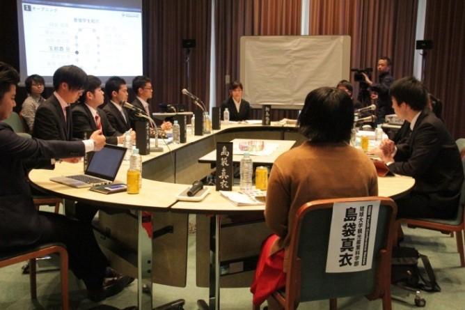 円卓会議にて、大学生の島袋 真衣さんとスーツの男性数名が会議を行っている写真