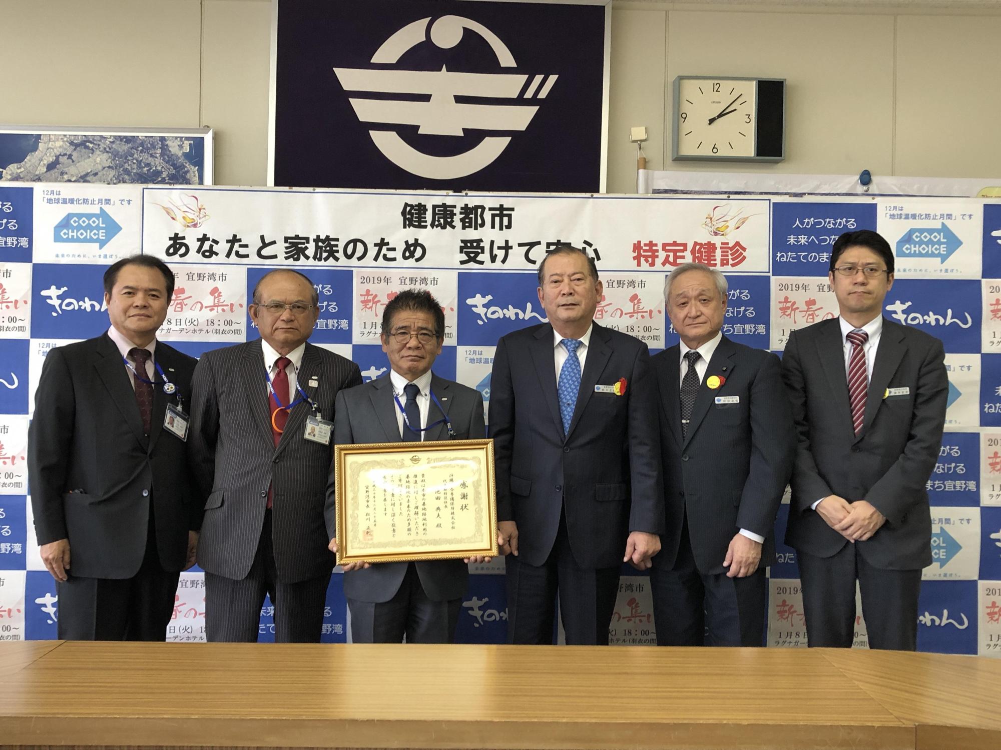 額縁に入った賞状を両手で持っている池田 典夫さんの右隣に松川市長が立ち、二人の両隣に関係者の方々が立っている集合写真