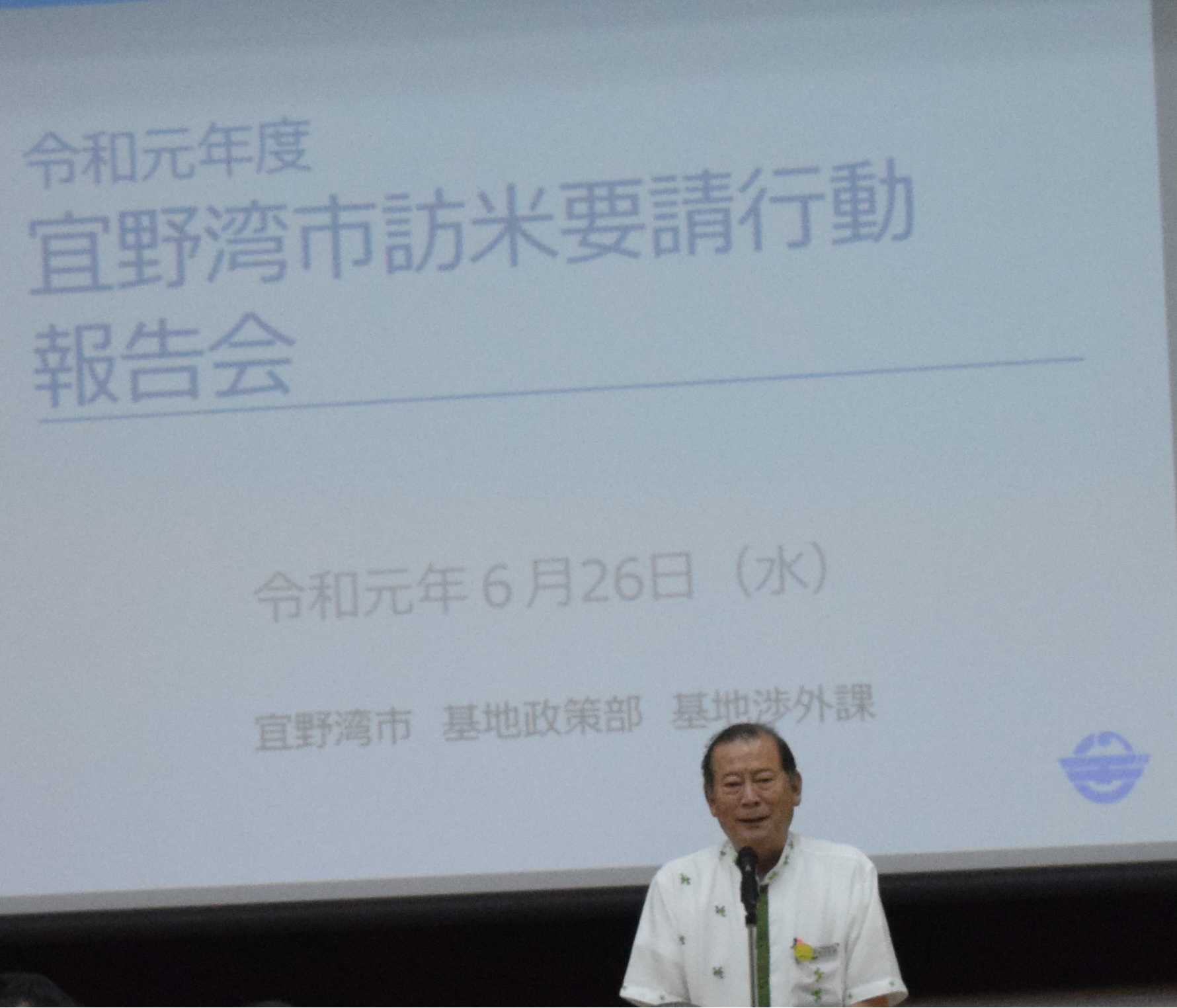 後ろには大きなスクリーンに資料が映し出されその前で松川市長が報告をしている写真