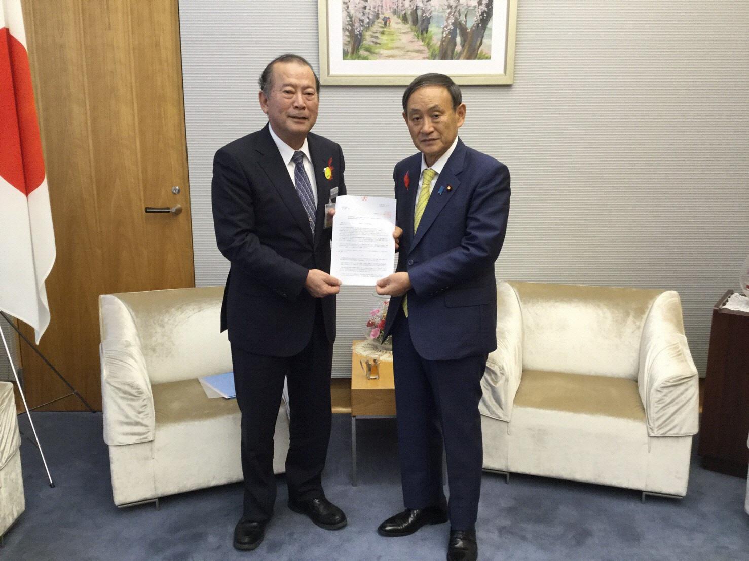 市長と菅官房長官が一緒に書類を持ちカメラの方に向けている写真