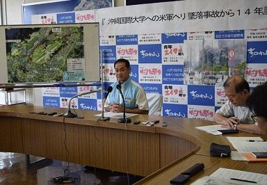 ホワイトボードには宜野湾の地図が貼られ宜野湾市長が椅子に座って記者会見をしている写真