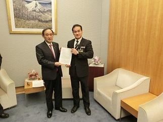 市長と菅官房長官が一緒に書類を持っている写真