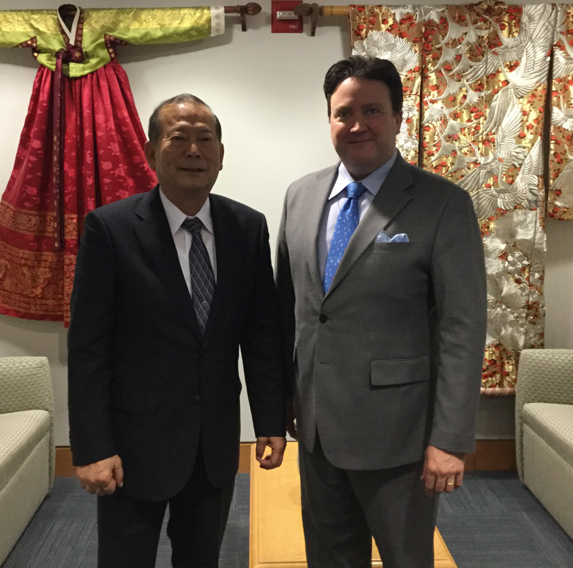 壁に日本の着物がかけられている前で日本人と国務次官補代理の男性が立っている記念写真