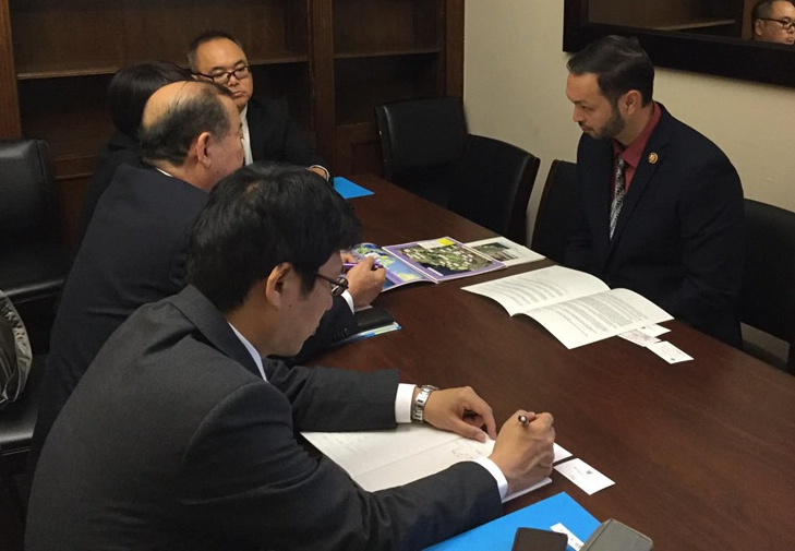 大きなテーブルを挟んで手前に日本人の男性2名と奥に1名、向かい側に下院代議員の男性が座って話をしている写真