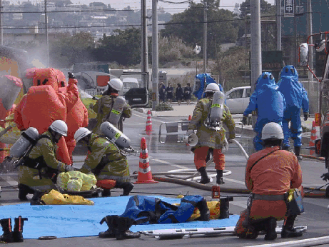 道路にブルーシートがひかれ消防隊員の人達が放水をしたり負傷者を担架にのせたり慌ただしく救助をしている写真