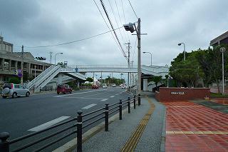 道路に沿って設置されているスロープから左前方に歩道橋が見え、青信号で車が走行している写真