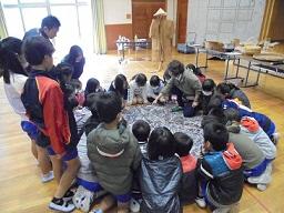 教室の真ん中に広げた資料を生徒達が囲んで円になって座って見ている写真