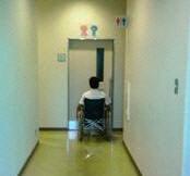 身障者用トイレ入り口前の車いすにのった男性の写真