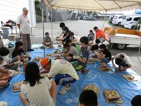 テントの中にビニールシートを広げて漆喰シーサーづくりをしている子供達の写真