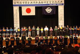 ステージ上に男女共同参画都市宣言記念式典と書かれた垂れ幕の下に参加者が横一列になって立っている写真
